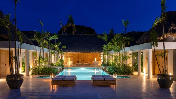 Un espace aménagé au bord de la piscine, avec des chaises longues, une structure à toit de chaume et des plantes tropicales.