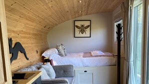 A cozy room with a wooden ceiling, a bed with white bedding, a grey sofa, a small desk, and a window with curtains. - Meadow View  - (Bottom Cabin)  - sleeps 2 guests  in 1 bedroom (Foolow)
