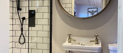 A modern bathroom with a glass-enclosed shower, a white sink with a gold faucet, and a round mirror on the wall.