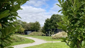 A grassy pathway leading to a small cabin surrounded by lush greenery. - Meadow View  - (Bottom Cabin)  - sleeps 2 guests  in 1 bedroom (Foolow)