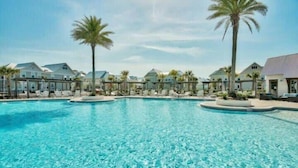 Ein großer, klarer Swimmingpool, umgeben von Liegestühlen und Palmen, mit Hotelgebäuden im Hintergrund.