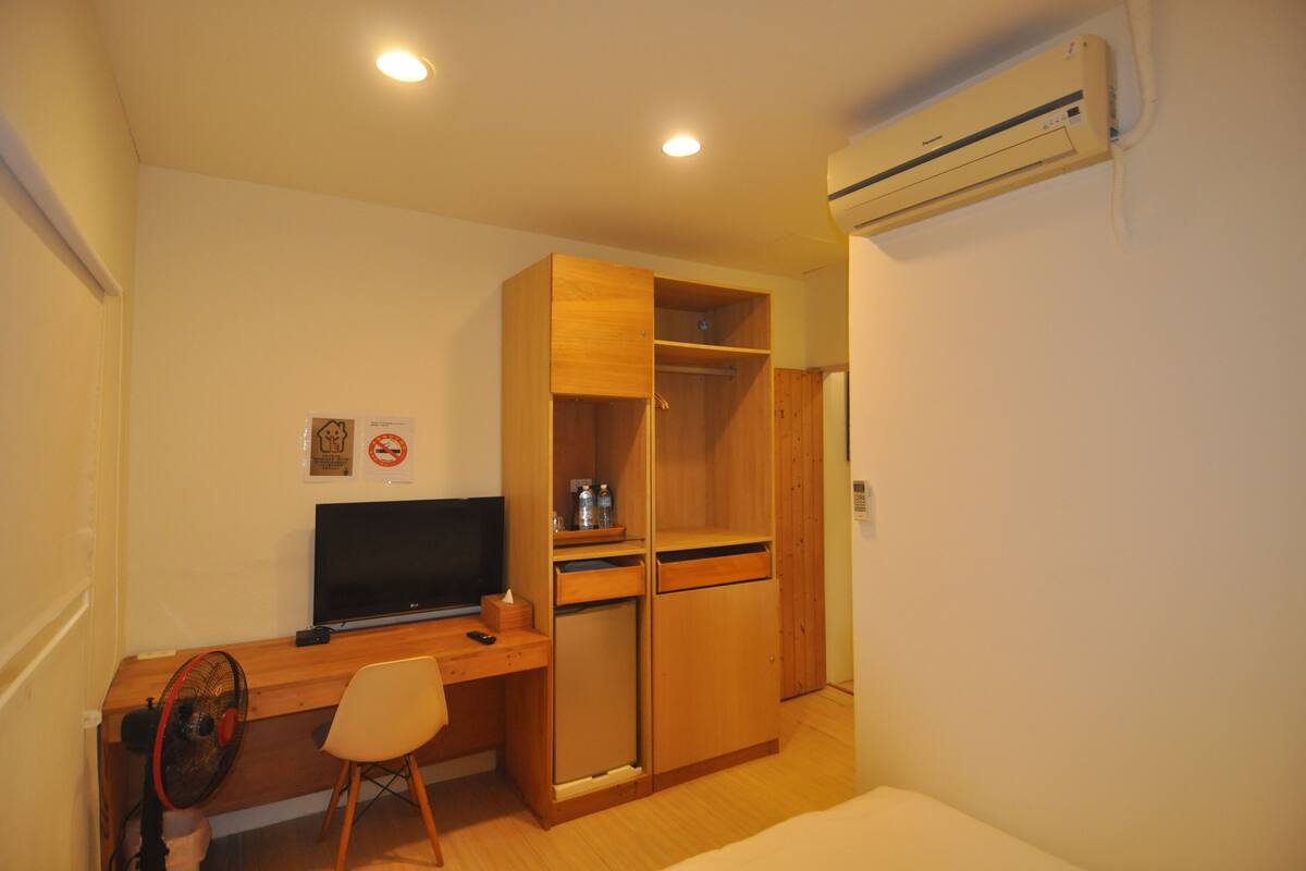 Una habitación compacta con escritorio de madera, una silla, televisor, refrigerador pequeño y armario.