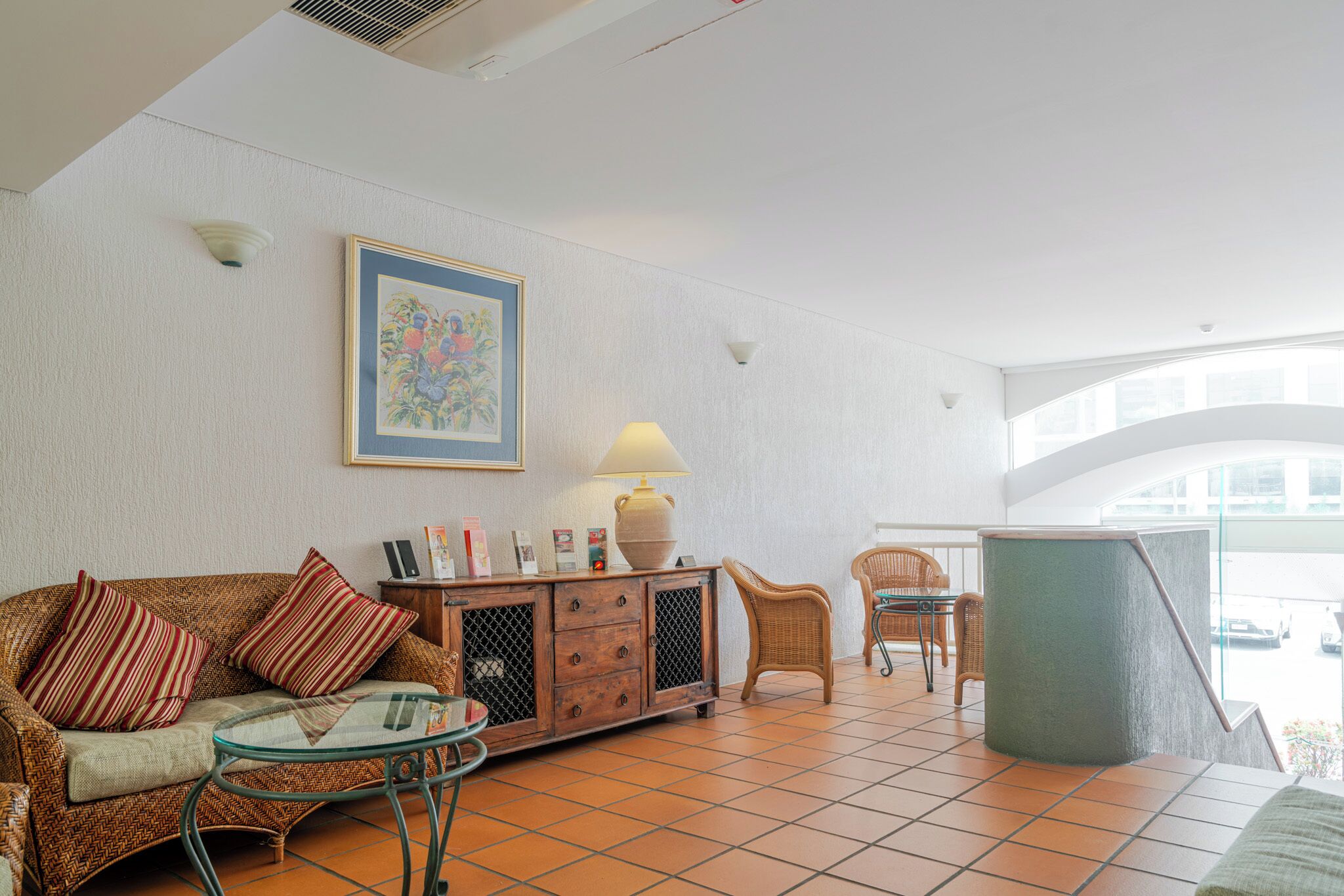 A room with a sofa, a glass table, a cabinet, wicker chairs, and a large window.