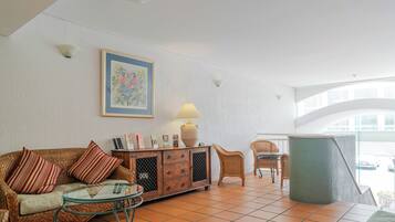 A room with a sofa, a glass table, a cabinet, wicker chairs, and a large window.