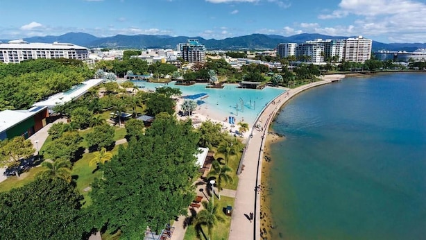 An aerial view of a coastal resort with a large pool area, beachfront promenade, and surrounding greenery. - Inner City One Bedroom Apartment with Pool View 22 (Cairns)