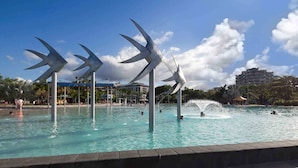 A swimming pool with large windmill sculptures, surrounded by a paved walkway and buildings in the background. - Inner City One Bedroom Apartment with Pool View 22 (Cairns)