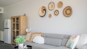 A modern living room with a grey sofa, a wooden cabinet, and wall-mounted woven art pieces. - Inner City One Bedroom Apartment with Pool View 22 (Cairns)