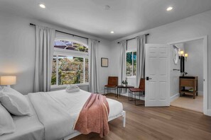 A bedroom with a bed, a desk, chairs, a window, and a door.