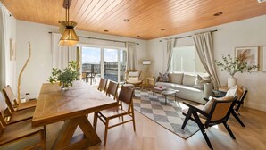 A spacious living area with a wooden dining table, comfortable seating, and large windows offering a view. - Voted Guest Favorite! Get Wow'd! Stellar Views Hollywood Hills (Los Angeles)