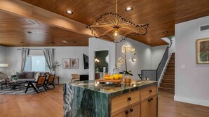 A spacious living area with a wooden ceiling, a marble island, and a staircase leading to an upper level. - Voted Guest Favorite! Get Wow'd! Stellar Views Hollywood Hills (Los Angeles)