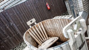 A wooden barrel-shaped trash bin with a metal handle, placed outdoors against a wooden fence. - Digby's Hut - sleeps 2 guests  in 1 bedroom (Foolow)