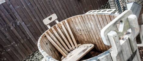 A wooden barrel-shaped trash bin with a metal handle, placed outdoors against a wooden fence.
