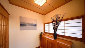 A traditional Japanese interior with a tatami mat floor, a shoji screen, a wooden bench, and a vase with branches. - TAKETORI ROTEN (Beppu)