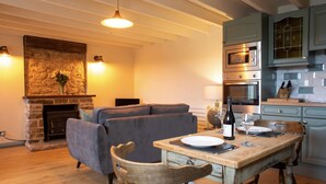 A cozy living room with a fireplace, a sofa, and a dining table set for two. - Brosterfield Cottage - sleeps 2 guests  in 1 bedroom (Foolow)