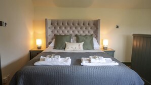 A neatly made bed with a tufted headboard, two bedside tables with lamps, and a set of folded towels on the bed. - Brosterfield Cottage - sleeps 2 guests  in 1 bedroom (Foolow)
