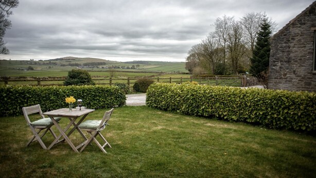 A rustic outdoor seating area with a table and chairs, surrounded by neatly trimmed hedges and a stone building. - Brosterfield Cottage - sleeps 2 guests  in 1 bedroom (Foolow)