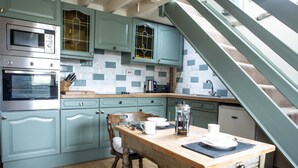 A kitchen with teal cabinets, a wooden table, and a coffee maker. - Brosterfield Cottage - sleeps 2 guests  in 1 bedroom (Foolow)