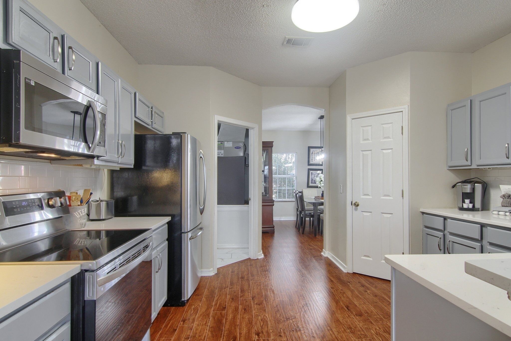 A modern kitchen with stainless steel appliances, wooden flooring, and light-colored cabinetry.
