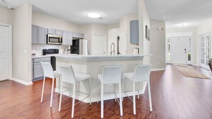 A modern kitchen with white cabinets, a central island with bar stools, and a large window. - Spacious 4 bedroom house by OWA & Tanger Outlets, 15 mins from Beaches (Foley)