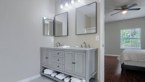 A bathroom with a gray vanity, two mirrors, a ceiling fan, and a window with a view of trees. - Spacious 4 bedroom house by OWA & Tanger Outlets, 15 mins from Beaches (Foley)