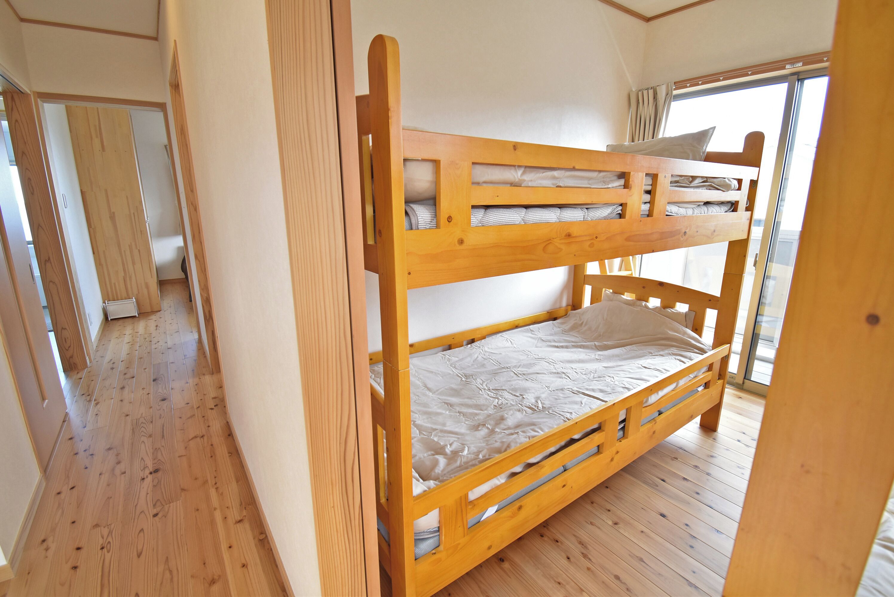 A bunk bed in a room with wooden flooring and a window.