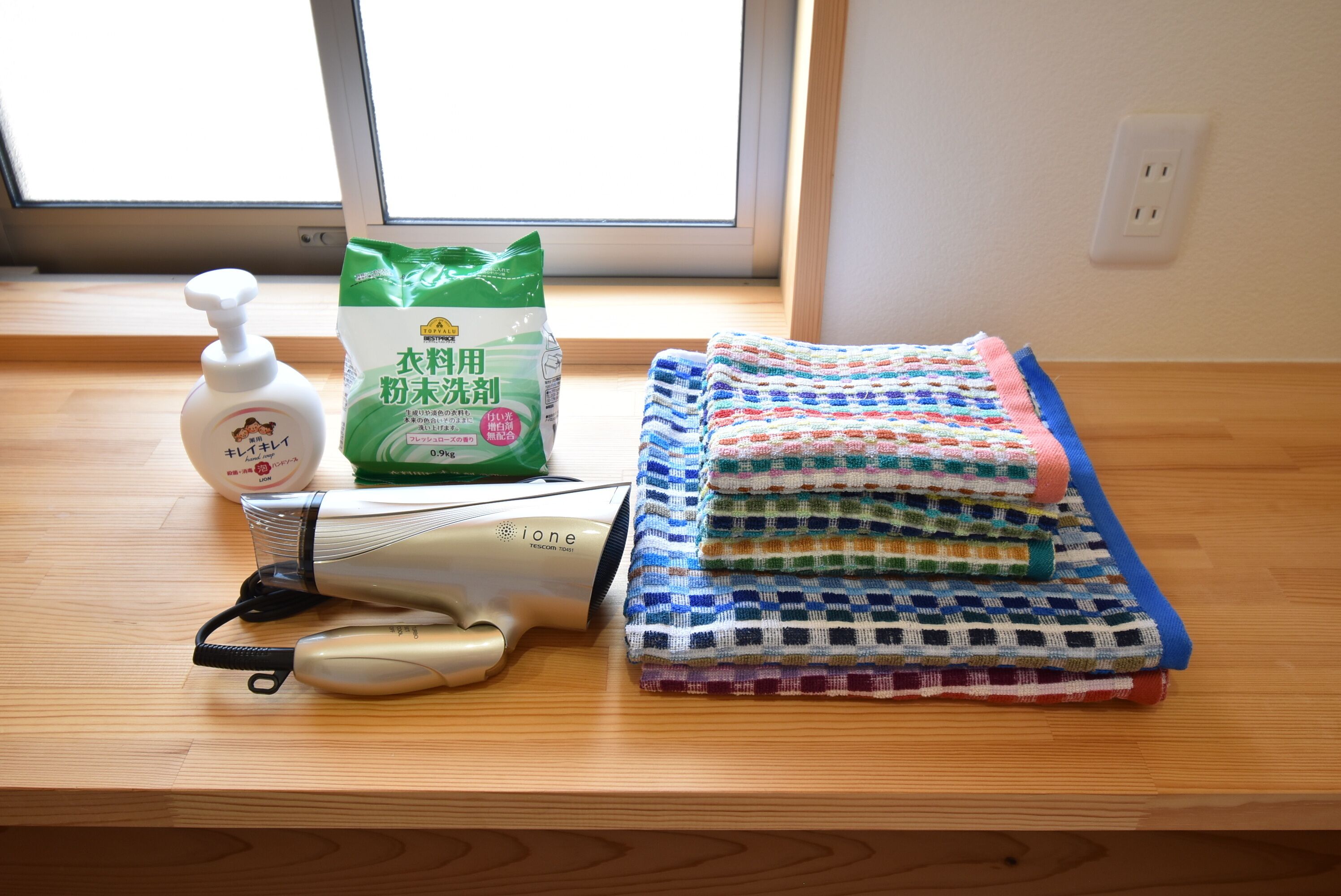A wooden table with a hairdryer, a bottle of hand soap, and a bag of laundry detergent.