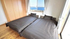 Ein Schlafzimmer mit zwei Betten, Holzboden, einem Kleiderschrank und einem Fenster mit Meerblick.