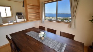 Ein Essbereich mit Holztisch, Stühlen, einer kleinen Küchenzeile mit Geräten und Blick auf das Meer durch ein großes Fenster.