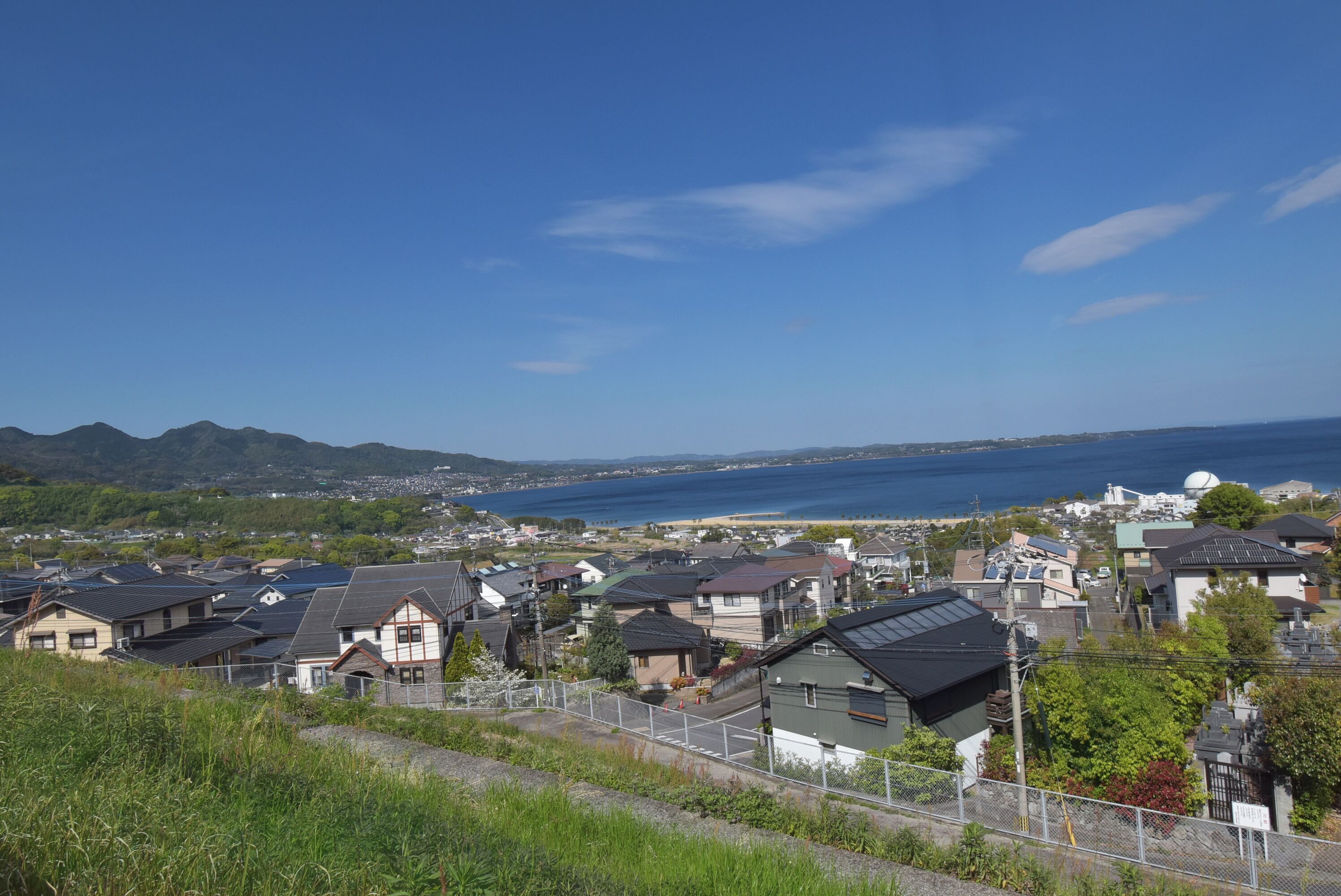 A residential area with houses, a clear sky, and a body of water in the distance.