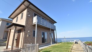Ein zweigeschossiges Haus mit Balkon, Meerblick und einem Rasenstück.