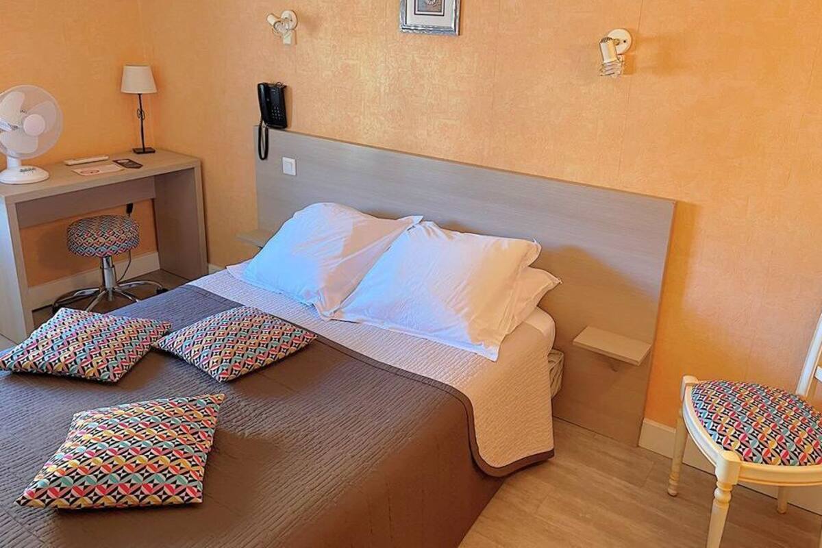 Une chambre d’hôtel avec un lit, une table de chevet, une chaise et un téléphone fixé au mur.