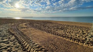 Une plage où l’on voit des traces de pneus et un ciel dégagé.