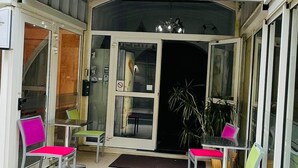 L’entrée de La Plage se distingue par son auvent blanc, ses portes vitrées et son espace extérieur aménagé avec des coussins aux couleurs vives.