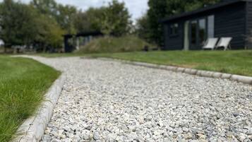 A gravel path leading to a modern building with a dark exterior and two lounge chairs visible.