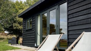 A modern building with large glass doors and a patio area with two lounge chairs. - Robin’s Nest - ( Top Cabin )  - sleeps 2 guests (Foolow)