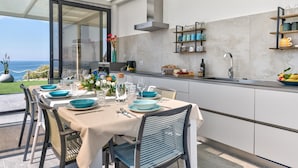 A modern kitchen with a dining area, a view of the sea, and a balcony with outdoor seating. - Villa Sabbie Rosse 6 2 (Isola di Capo Rizzuto)
