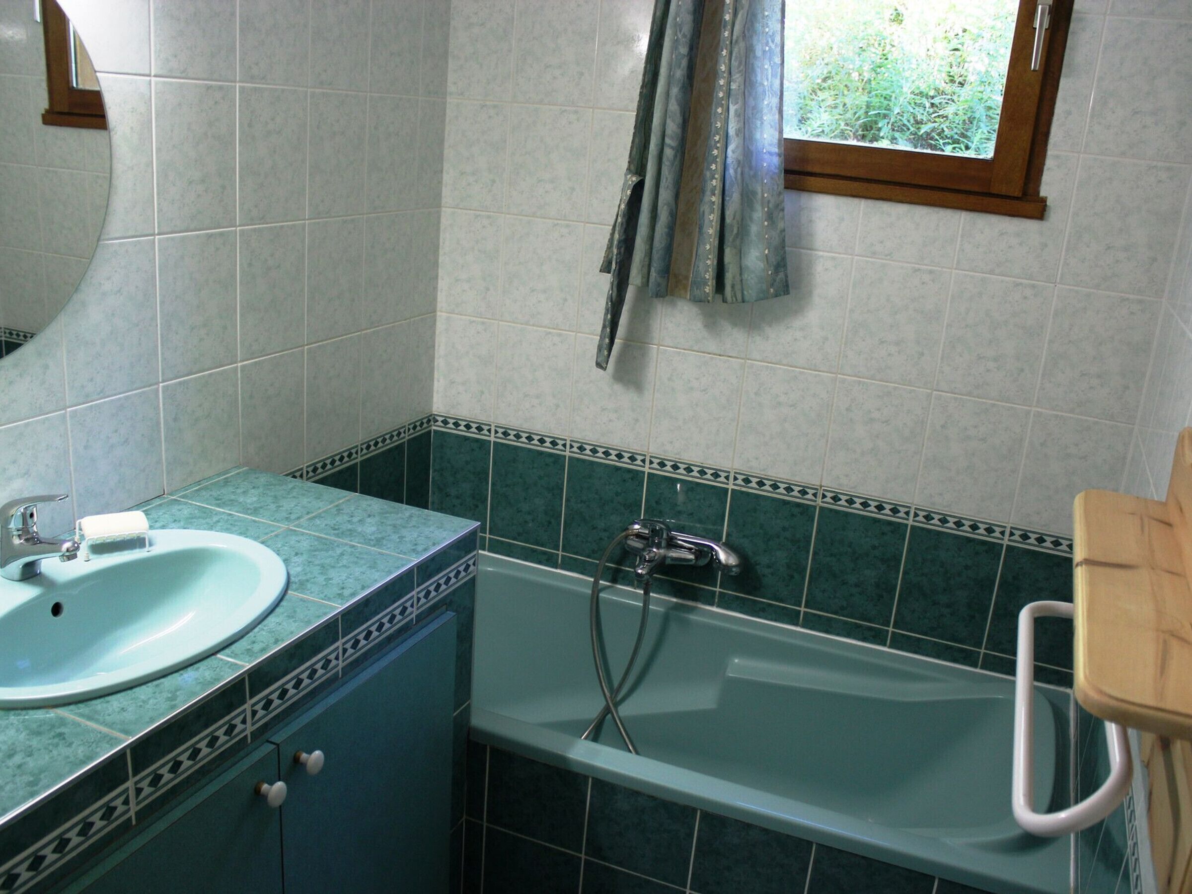 A bathroom with a sink, mirror, bathtub, and a window with curtains.