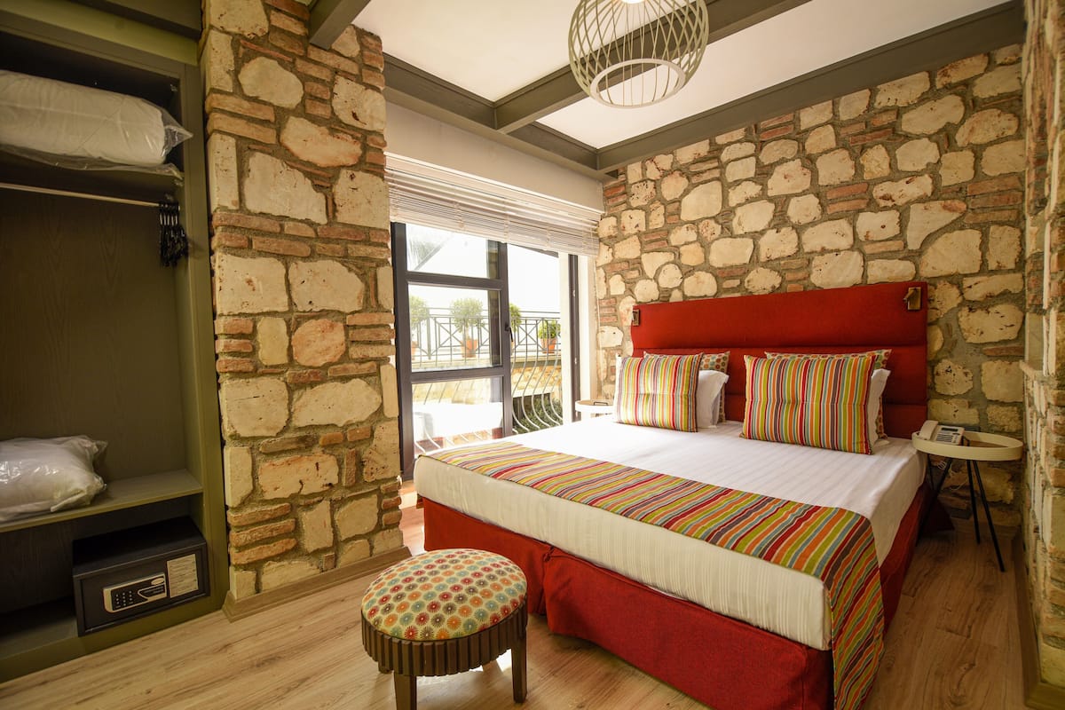 Une chambre avec un mur en pierre, une tête de lit rouge, une couvre-lit à rayures et un plancher en bois.