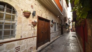 A narrow cobblestone street with stone buildings, a wooden door, and hanging flower pots. - Alp Pasa Fiore Garden Suites - Special Class (Antalya)
