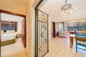 Amplia sala de estar con piso de madera, un sofá, una mesa de comedor y una cama con almohada a rayas.