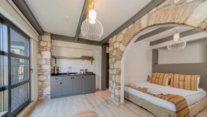 A cozy bedroom with a bed, a small stool, and a kitchenette in the background. - Alp Pasa Fiore Garden Suites - Special Class (Antalya)