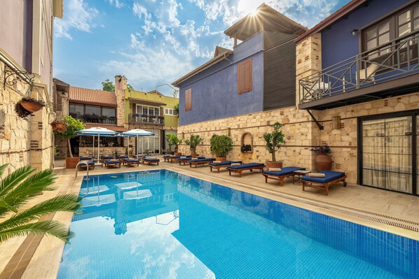 Una piscina con sillas de descanso y sombrillas, rodeada de edificios con fachadas de piedra y balcones.
