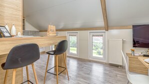 Une cuisine moderne avec des meubles en bois, un plan de travail et des tabourets de bar. Une grande fenêtre offre une vue sur la verdure environnante.