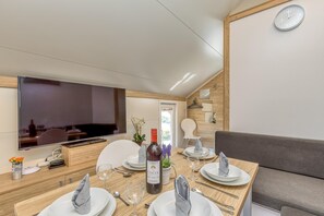 A modern dining area with a wooden table set for four, a bottle of wine, and a television on the wall.