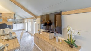 Une cuisine moderne avec des meubles en bois, un grand téléviseur à écran plat et un coin repas avec une table mise pour deux personnes.