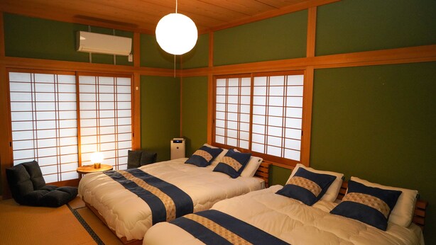 Ein traditioneller japanischer Raum mit zwei Betten, Tatami-Boden, Shoji-Schiebetüren und einem Deckenventilator.