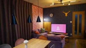 Ein modernes Wohnzimmer mit einer Couch, einem Holztisch und einem Fernseher, der das Airbnb-Logo zeigt.