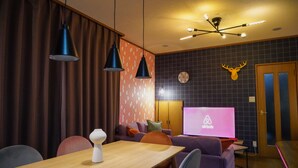 Ein modernes Wohnzimmer mit einem Holztisch, einem violetten Sofa und einem Fernseher, der das Airbnb-Logo zeigt.