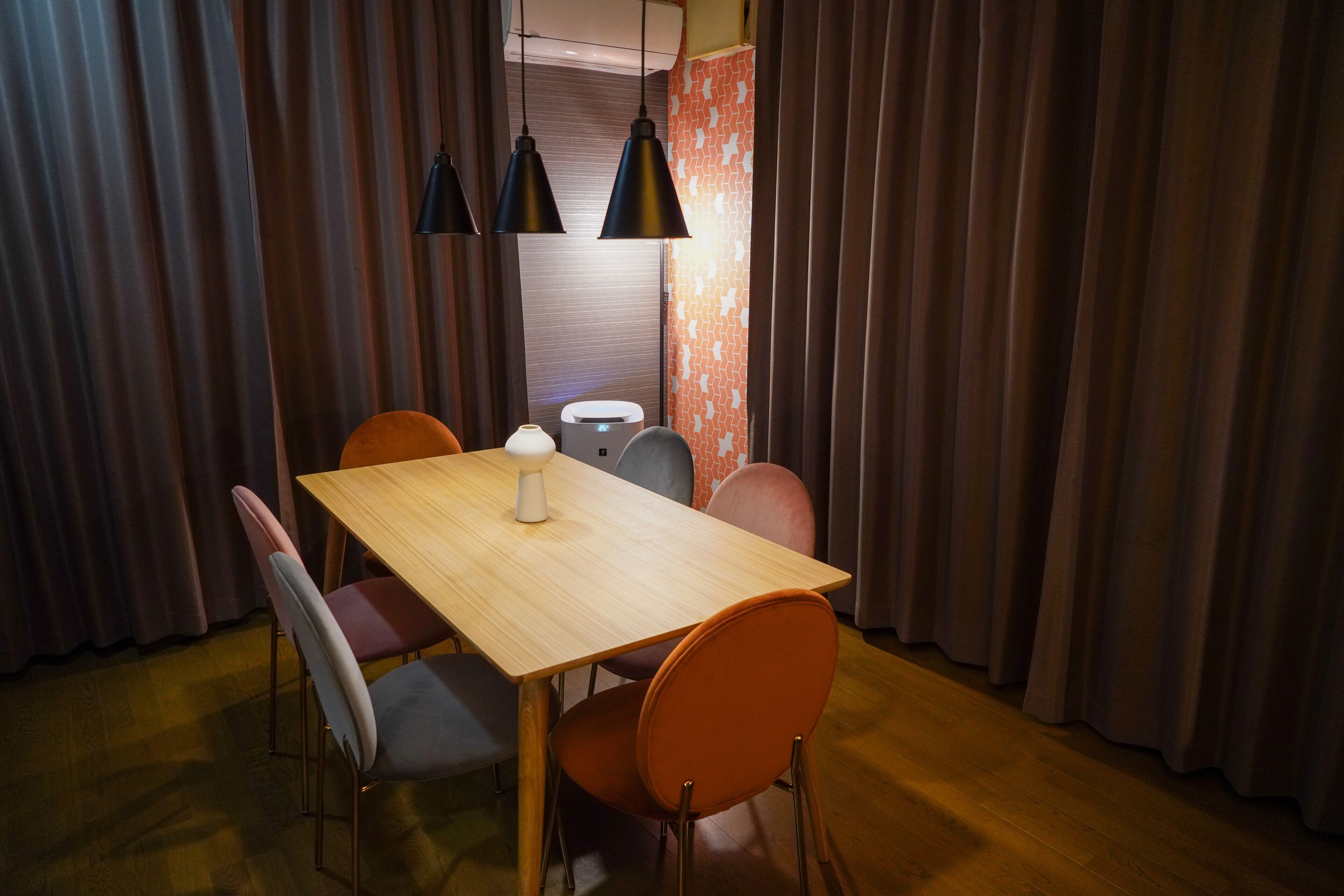 A dining area with a wooden table, orange chairs, and black pendant lights.