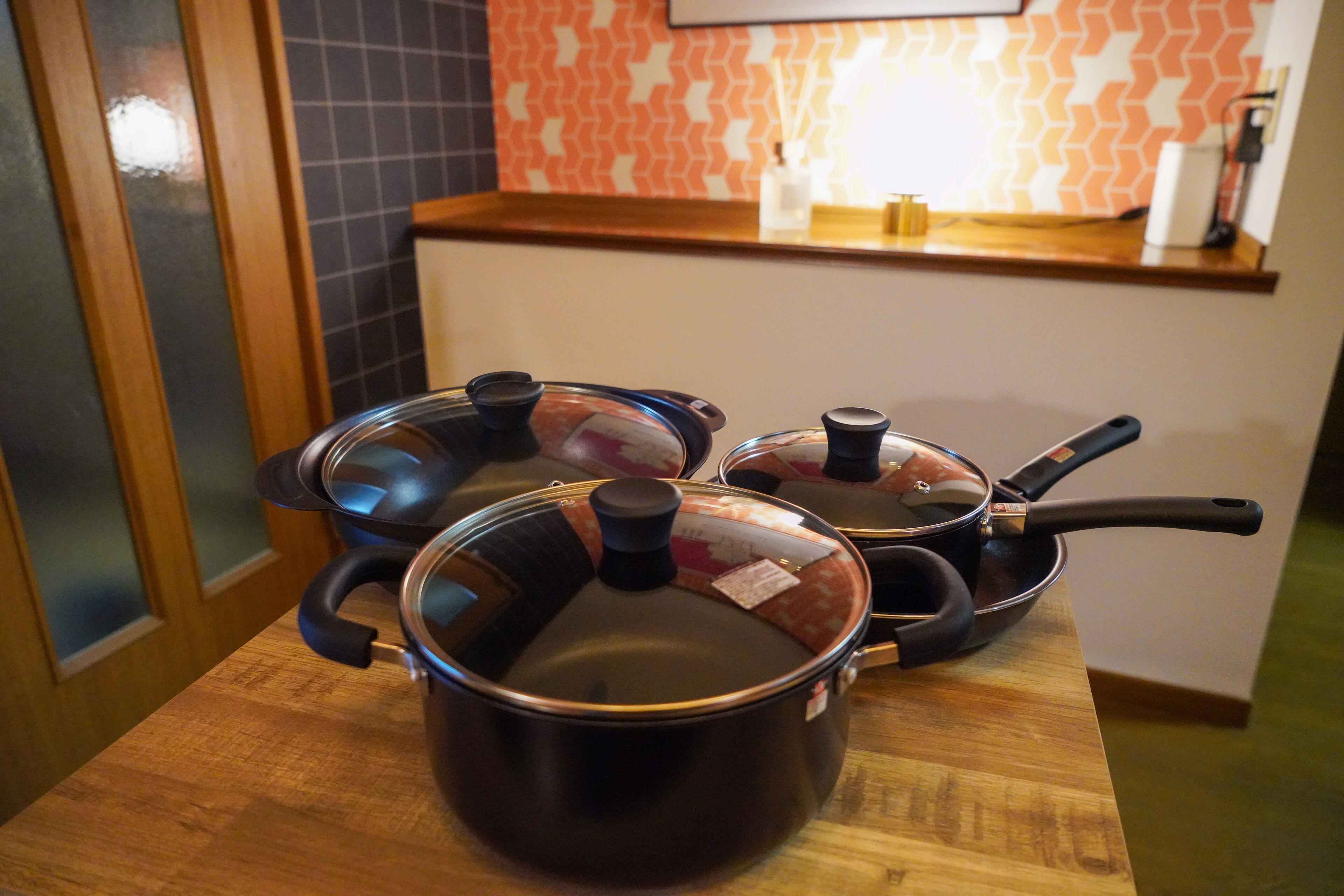 Une cuisine avec trois casseroles sur un plan de travail en bois, un pare-feu en carreaux et une porte en bois.